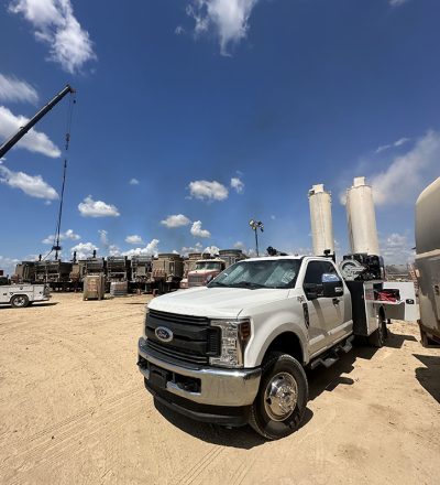 A truck parked in a dirt lot beside a crane