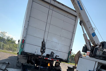 A crane lifts a large truck onto a flatbed