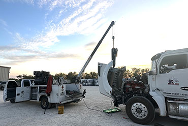 In a parking lot, a crane hoists a truck